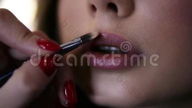 非常接近镜头化妆师涂口红刷在嘴唇年轻的女人。 工艺应用唇彩